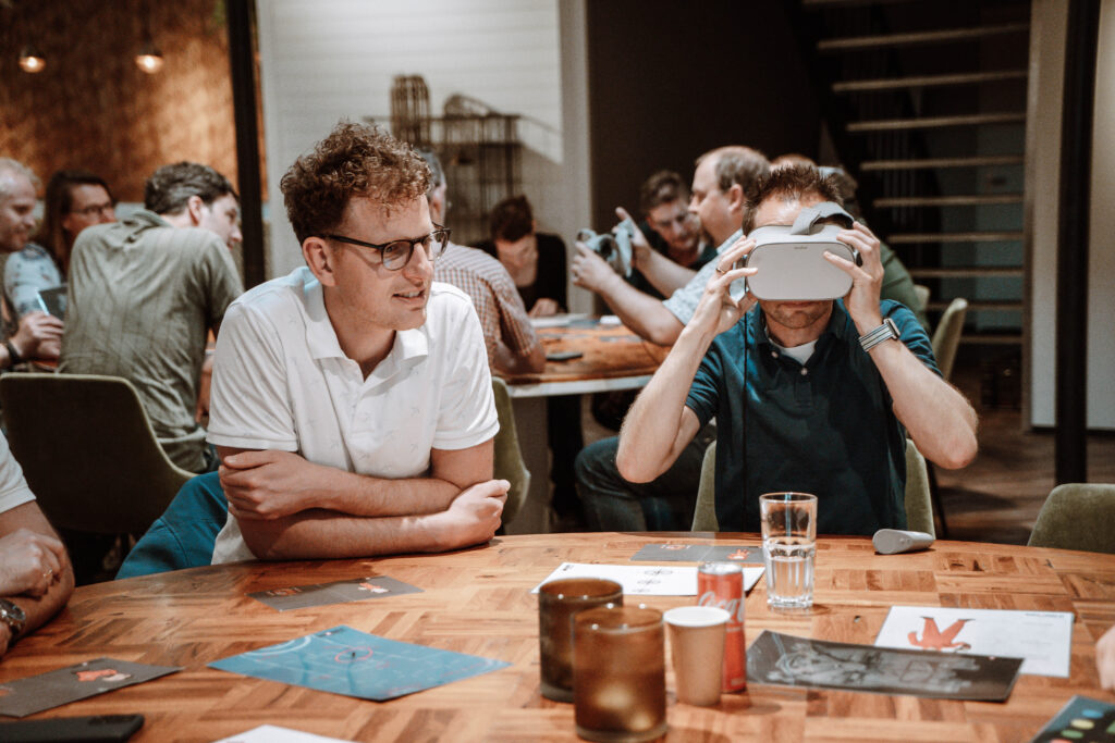 Mannen werken samen in Mission Metaverse, een in het echt en een met VR-bril.
