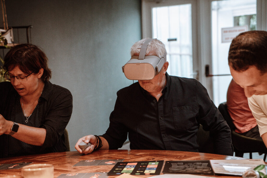 Man met VR-bril, terwijl de groep bezig is met puzzels in het echt.